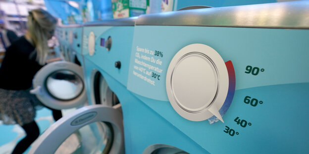 Eine Frau befüllt eine Waschmaschine. Im Vordergrund ist ein Temperaturregler zu sehen, auf 30 Grad gestellt.