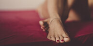 Eine Person mit rot lackierten Fußnägeln liegt nackt auf einem roten Bettlaken
