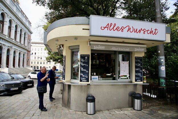 Ein Wurststand, davor ein paar Kunden, darüber der Schriftzug 