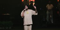 Emicida im schicken ockerfarbenen Trainingsanzug auf einer Bühne am Mikrofon