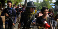 Junge bewaffnete Rebellen marschieren in einem Protestmarsch mit, bei der ein Demonstrant ein Megafon hält.
