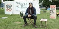 Aktivist Henning Jeschke sitzt beim Hungerstreik vor Bannern auf einer Wiese im Regierungsviertel