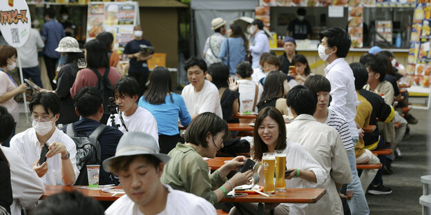 Japanese people sit on wooden benches and drink beer