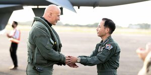 Zwei Männer in Militäranzügen begrüßen sich auf einem Flugplatz