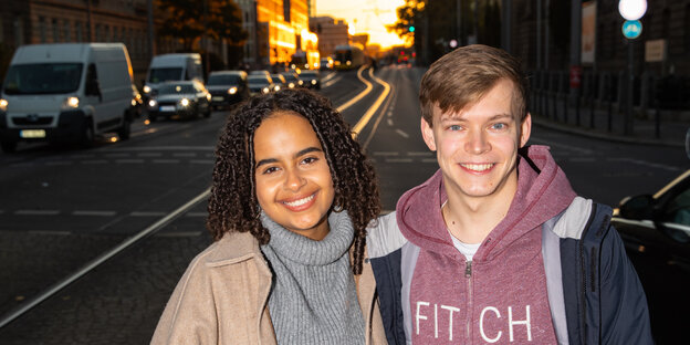 Sarah-Lee Heinrich und Timon Dzienus stehen auf einer dunklen Straße und lachen in die Kamera