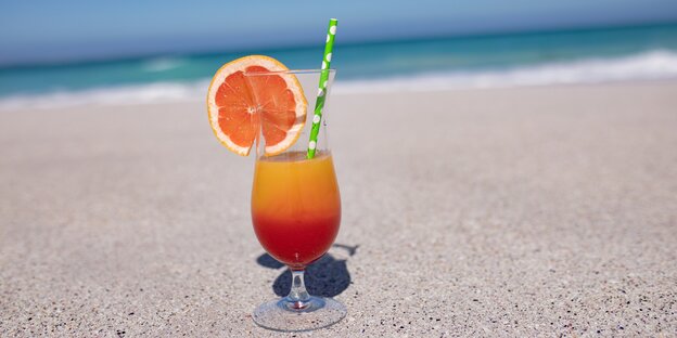 Ein orangeroter Cocktail im Glas auf einem Strand