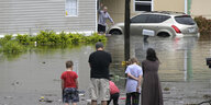 Fünf Menschen verschiedenen Alters stehen voir einer überfluteten Straße