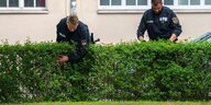 Zwei Polizist*innen des Bundeslands Bremen durchsuchen eine Hecke