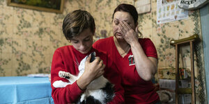 Ein Junge umarmt eine Katze, daneben sitzt eine verzweifelte Frau