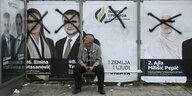 Ein Mann sitzt an einer Bushaltestelle. Hinter ihm Wahlplakate auf denen die Gesichter mit Farbe beschmiert wurden.