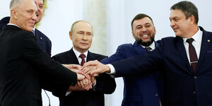 Eine Gruppe von Personen um Wladimir Putin türmt ihre Hände übereinander