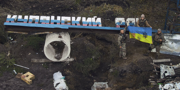 Soldaten und ein kaputtes Schild, auf dem in Kyrillisch Kupjansk steht