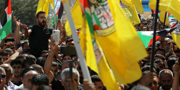 Ein junger Mann, sichtlich empört, ragt aus der Menge der Trauernden die mit gelben Flaggen unterwegs sind