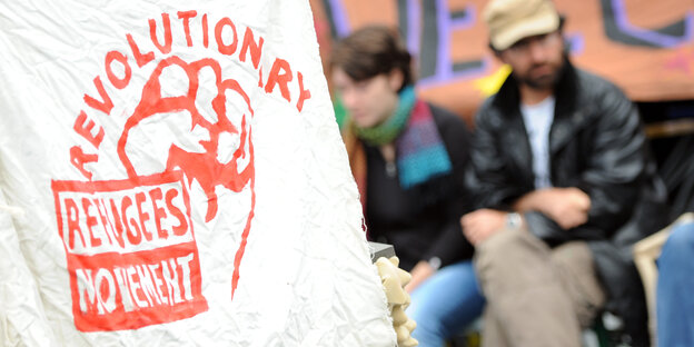 Ein Banner mit der Aufschrift "Radical Refugee Movement", Im Hintergrund sitzt ein unscharfer Mann