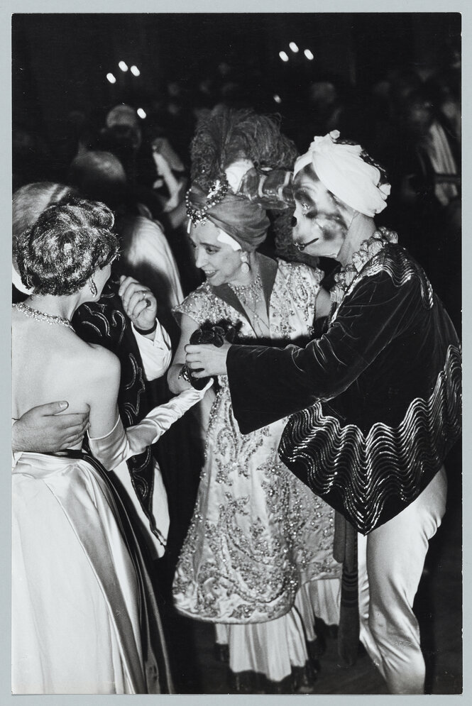 Schwarzweiß Fotografie einer Ballszene von 1952, Elsa Schiaparelli in einem bestickten Kostüm, ihr Tanzpartner mit Maske und einem mit Wellen bestickten weiten Umhang