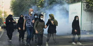 Junge Menschen mit Gesichtsmasken gehen an Tränengasschwaden vorbei