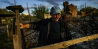 Ein Mann steht hinter einem Holzzaun. Hinter ihm sind zerstörte Gebäude zu erkennen.