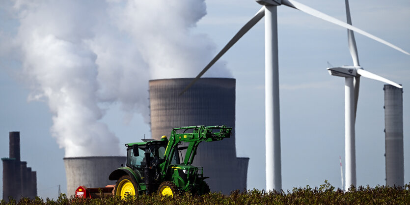 Ein Traktor auf einem Feld, im Hintergrund rauchende Kühltürme eines Kraftwerks und Windräder