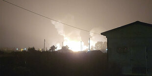 Ein Feuer im Hintergrund der Nacht, vorn der Schatten eines Hauses