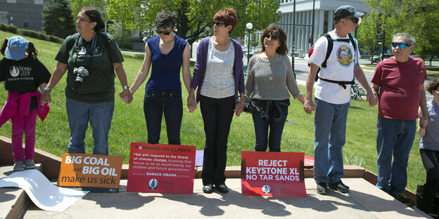 Demonstraten halten sich an den Händen, zu ihre Füßen haben sie Schilder aufgestellt: Reject Keystone XL