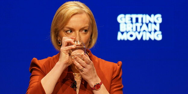 Liz Truss hält mit zwei Händen Wasserglas, um zu trinken