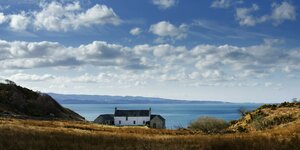Ein einsamer Drei-Seiten-Hof in den Hügeln der Hebriden, dahinter das Meer