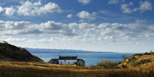 Ein einsamer Drei-Seiten-Hof in den Hügeln der Hebriden, dahinter das Meer