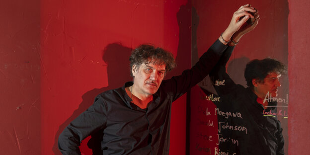 Frank Spilker steht vor einer roten Wand und lehnt sich an einen beschriebenen Spiegel
