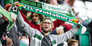 Ein Vfl Wolfsburg Fan hält einen Schal seiner Lieblingsmannschaft in die Höhe