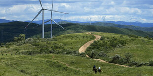 Zwei Reiter unterwegs in einer hügeligen Landschaft in der viele Windräder rumstehen