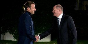 Emmanuel Macron und Olaf Scholz schütteln sich die Hände und lächeln sich an