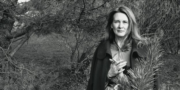 Annie Ernaux steht im Jahr 2002 zwischen Nadelbäumen - schwarz-weiss Aufnahme