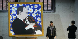 Ein Gemälde zeigt Wladimir Putin der mit einem kleinen Hund kuschelt vor blauem Hintergrund mit Margeritenblüten