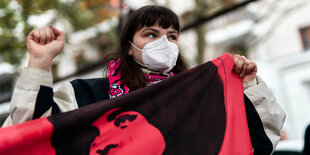 Eine junge Frau mit Gesichtsmaske und erhobener Faust hält ein Banner in der Hand