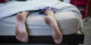 Junger Mann liegt im Bett, es sind nur seine ungewaschenen Füße zu sehen