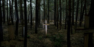 Holzkreuze stehen auf Gräbern im Wald