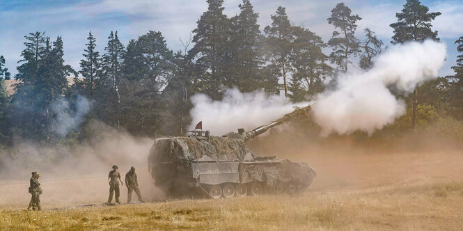 Panzer mit Rauch auf einem Stoppelfeld, Soldaten dahinter