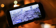 Ein Smarthphone wird in der Hand gehalten auf dem der Telegram Kanal Nexta eine Protestaktion live überträgt