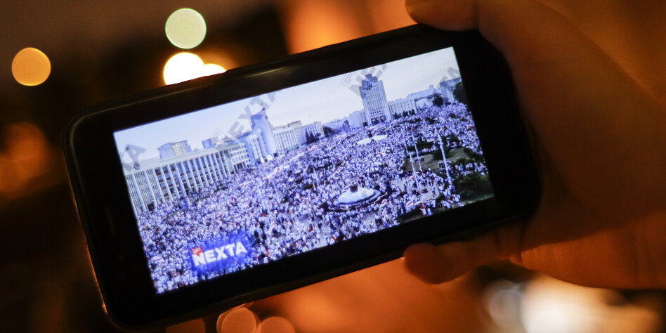 Ein Smarthphone wird in der Hand gehalten auf dem der Telegram Kanal Nexta eine Protestaktion live überträgt