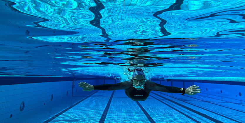 Ein Mann schimmt im Neoprenanzug und mit Badekappe im Freibad