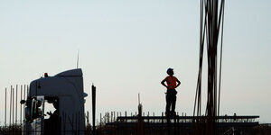 HInter einem LKW blickt ein Arbeiter an einem Bündel Bewehrungsstahlruten hoch