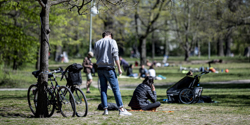 Menschen sitzten und stehen auf einer Wiese, Fahrräder, Bäume