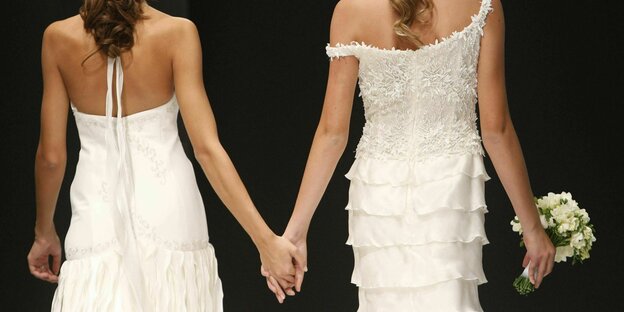 Zwei Frauen in Hochzeitskleidern halten Händchen