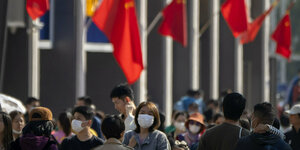 Menschen tragen Masken in einer vollen Einkaufsstraße in Peking