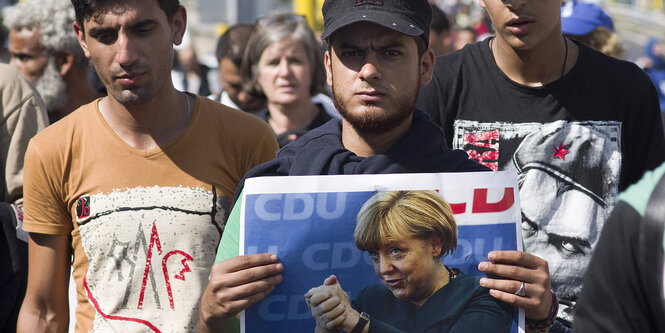 Ein Mann hält ein Plakat mit einem Foto von Angela merkel