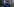 Mark Fell mit Rucksack in einem Wald, im Hintergrund sind schemenhafte Lichter zu sehen