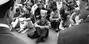 Ein Sitzstreik, eine Person hat sich eine Papiertüte über den Kopf gestülpt auf der das Gesicht des persischen Schas zu sehen ist