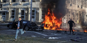 Männer stürzen an einem brennenden Auto vorbei