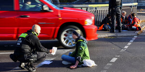 Ein Polizist redet mit einem Menschen, der sich auf der Straße festgeklebt hat