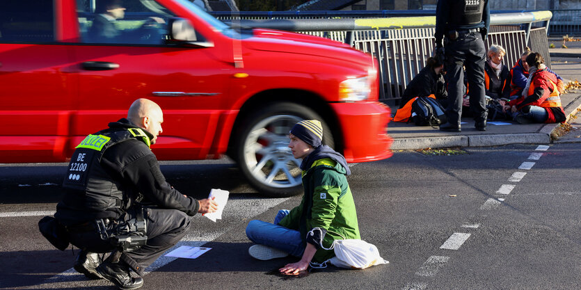 Ein Polizist redet mit einem Menschen, der sich auf der Straße festgeklebt hat